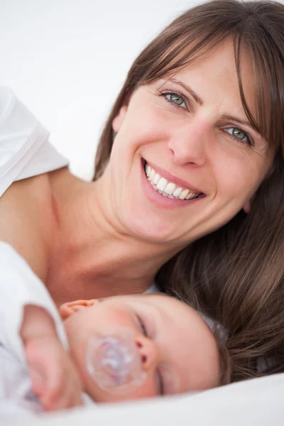 Mujer morena sonriente acostada mientras su bebé duerme — Foto de Stock