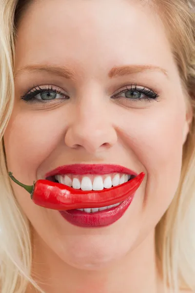 Mulher loira alegre colocando um chili entre os dentes — Fotografia de Stock