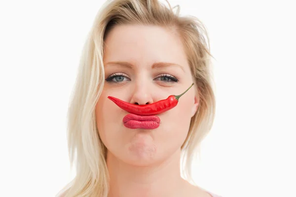 Blonde woman placing a chili between her nose and her mouth — Stock Photo, Image