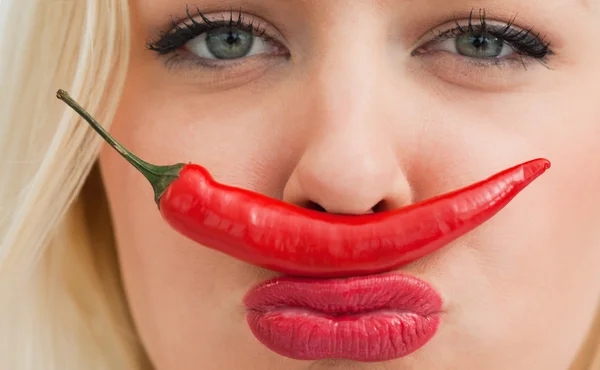 Jonge vrouw plaatsen een chili tussen haar neus en haar mond — Stockfoto