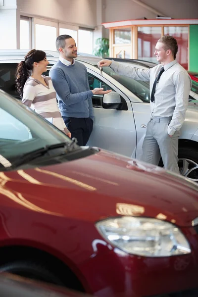 Smiling salesman giving keys to a happy couple — Stock Photo, Image