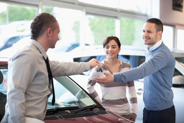 Smiling couple receiving keys from a car dealer — Stock Photo, Image