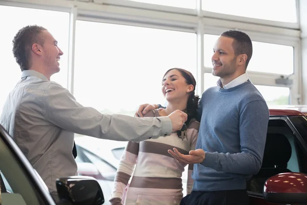 Laughing couple receiving keys from a salesman — Stock Photo, Image