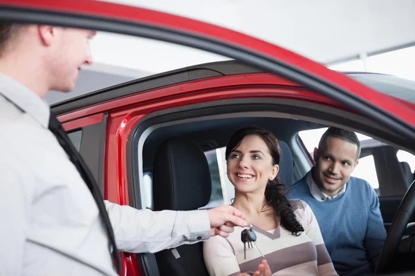 Pareja sentada en un coche recibiendo la llave de un concesionario de coches — Foto de Stock