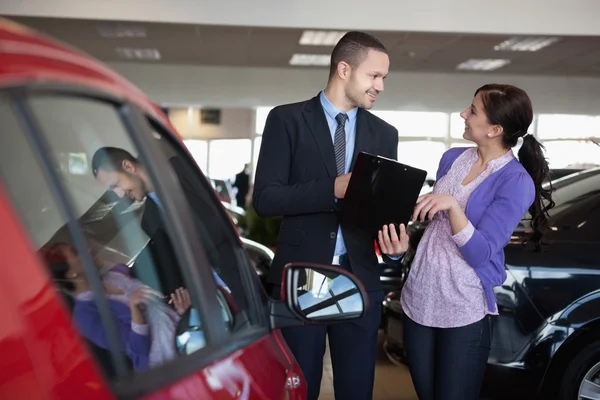 Salesman talking to a smiling woman next to a car — Stock Photo, Image