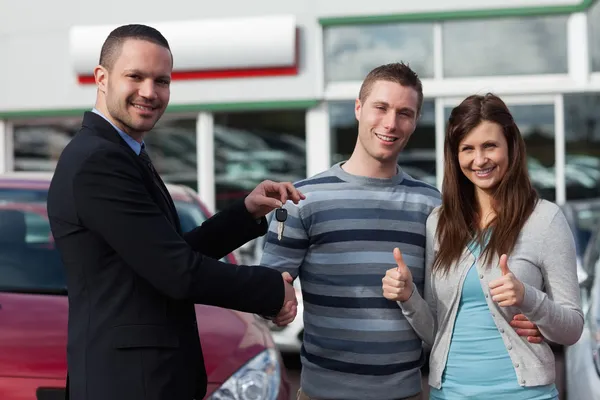 Distribuidor estrechando la mano de un hombre mientras le da las llaves del coche — Foto de Stock