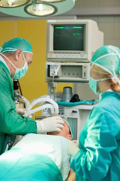 Paciente acostado en una mesa de operaciones con dos cirujanos — Foto de Stock