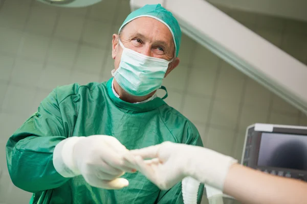 Lächelnder Chirurg nimmt ein Werkzeug aus einer behandschuhten Hand — Stockfoto