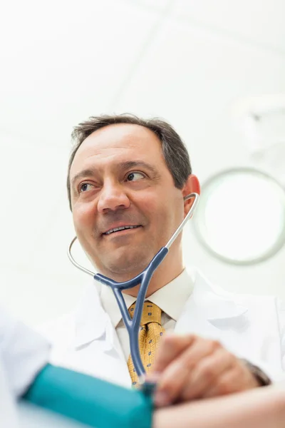 Médico sorridente medindo a pressão arterial de seu paciente — Fotografia de Stock