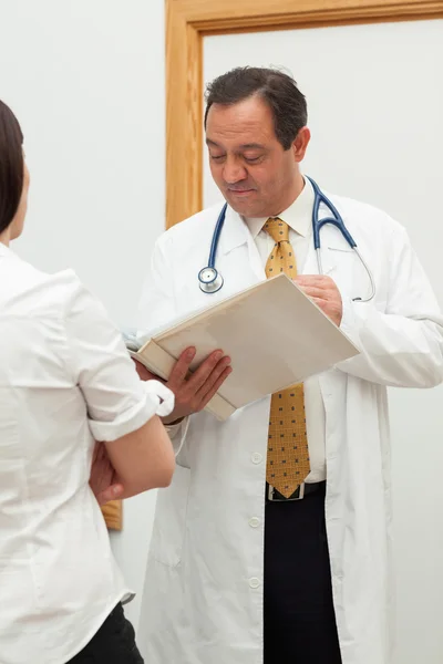 Médico olhando para um arquivo enquanto fala com uma mulher — Fotografia de Stock