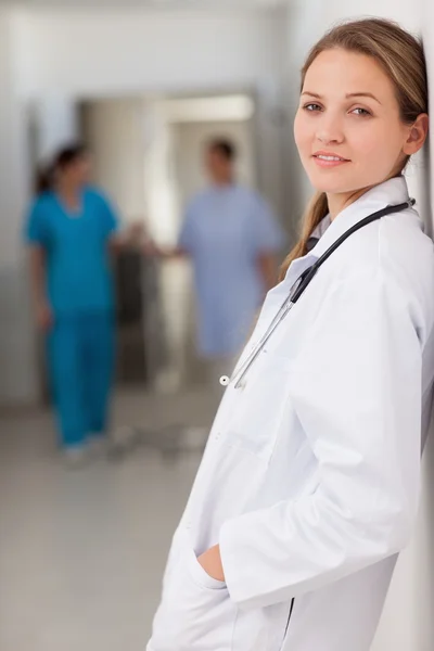 Lächelnde Ärztin, die mit den Händen in der Hosentasche vor einer Wand steht — Stockfoto