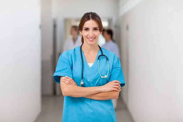 Sorridente infermiera piegando le braccia mentre in piedi — Foto Stock