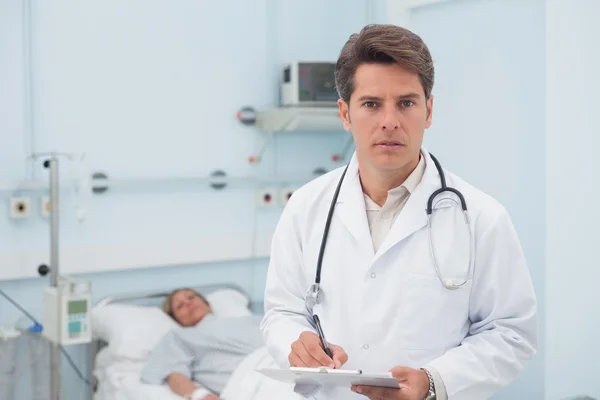 Doctor writing while holding a chart — Stock Photo, Image