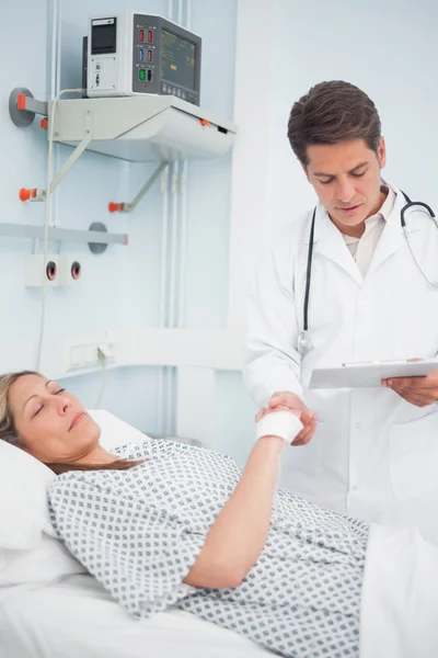 Arzt schaut auf sein Diagramm, während er die Hand seines Patienten hält — Stockfoto