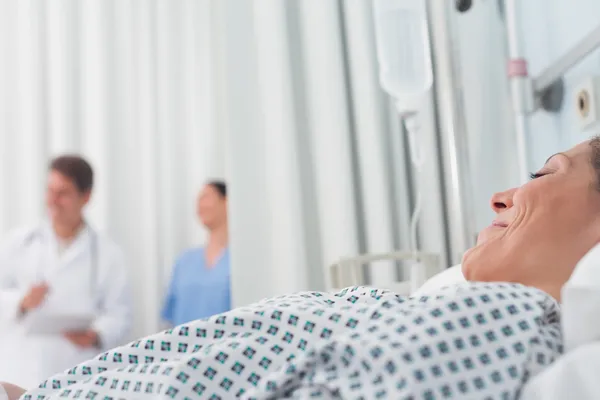 Paciente deitado em uma cama médica ao lado de um médico e uma enfermeira — Fotografia de Stock