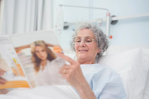 Elderly patient reading a magazine on her bed — Stock Photo, Image