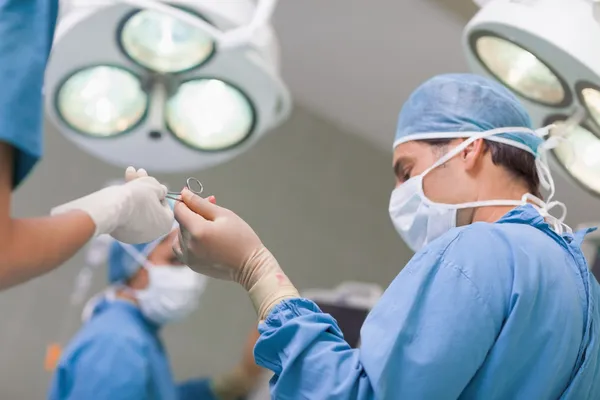 Doctor receiving a surgical scissor from a nurse — Stock Photo, Image