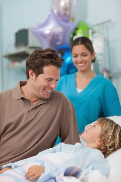 Ребенок лежит на медицинской кровати и смотрит на своего отца — стоковое фото