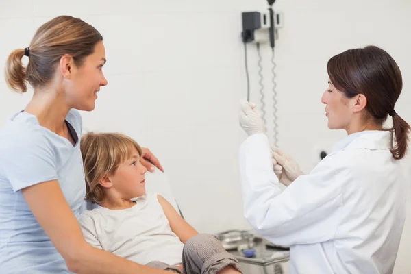 Arts voorbereiding van een injectiespuit naast een kind en zijn moeder — Stockfoto