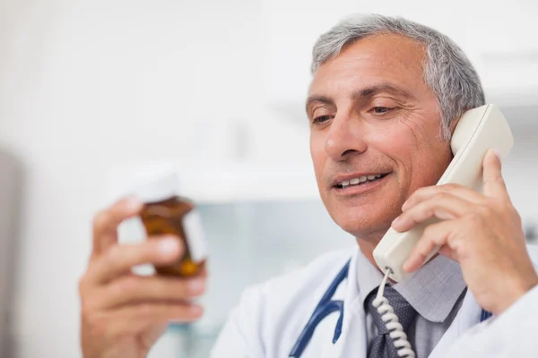 Arzt schaut beim Anruf auf eine Drogenflasche — Stockfoto