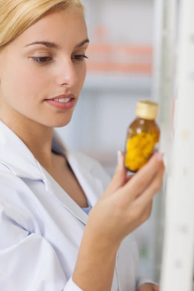 Farmacêutico loiro olhando para uma garrafa de droga — Fotografia de Stock