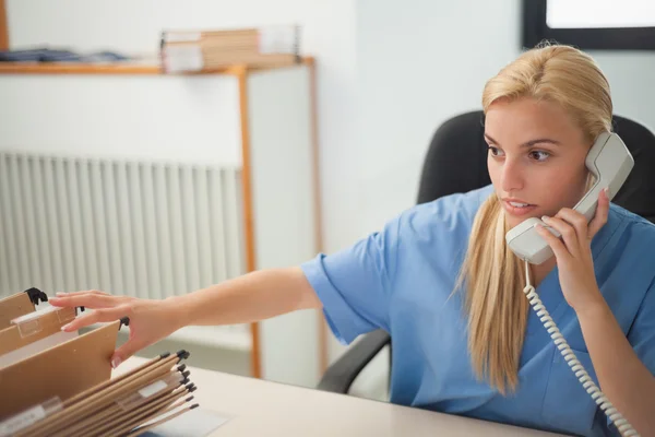 Enfermera sosteniendo un teléfono mientras busca en una carpeta —  Fotos de Stock