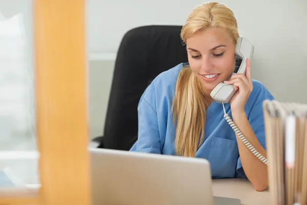 Enfermeira loira chamando ao lado de um laptop — Fotografia de Stock