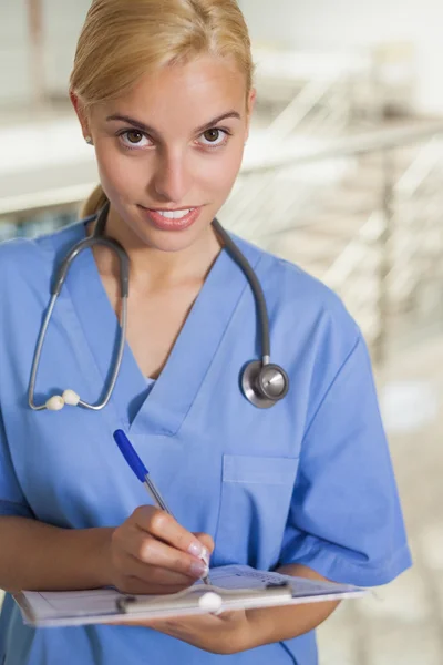 Krankenschwester schreibt auf Klemmbrett, während sie in die Kamera schaut — Stockfoto