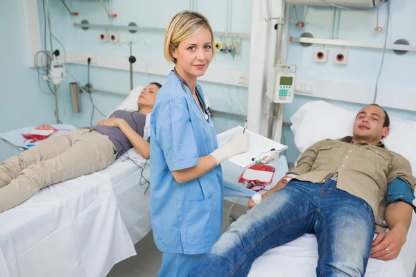 Two patients lying on bed next to a nurse — Stock Photo, Image