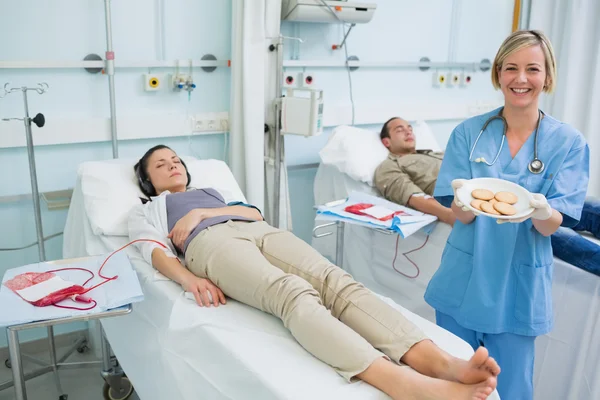 Enfermeira segurando uma placa de biscoitos ao lado de pacientes transfundidos — Fotografia de Stock