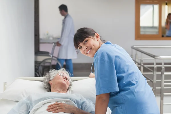 Leende sjuksköterska lutar på sängen av en patient — Stockfoto