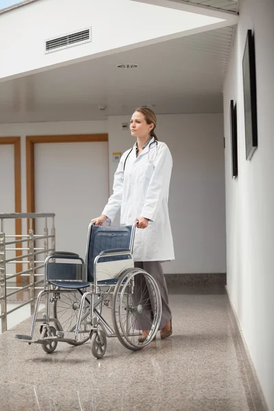 Médico serio empujando una silla de ruedas en el pasillo —  Fotos de Stock