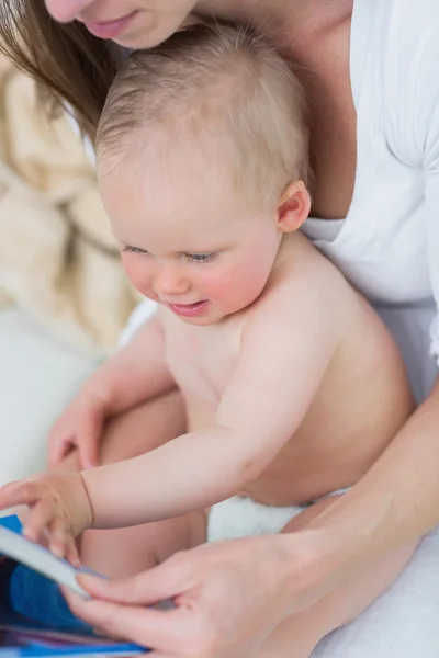 Baby sitzt auf seiner Mutter und schaut sich ein Buch an — Stockfoto