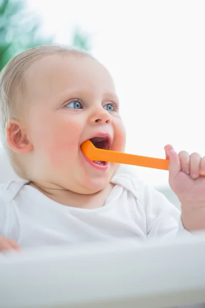 Bebê segurando uma colher de plástico em sua boca — Fotografia de Stock