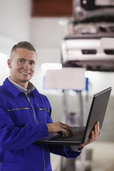Smiling mechanic typing on a laptop — Stock Photo, Image