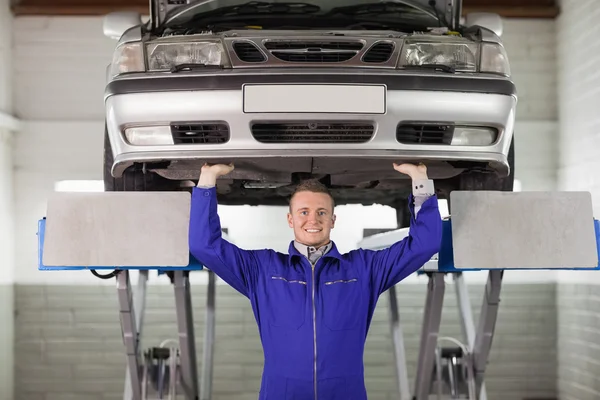 Mecánico sonriente tocando la parte inferior de un coche — Foto de Stock