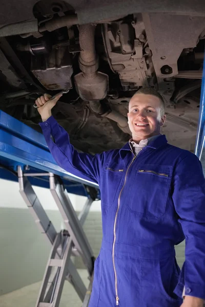 Mecânico sorrindo reparação com uma chave de chave o abaixo de um carro — Fotografia de Stock