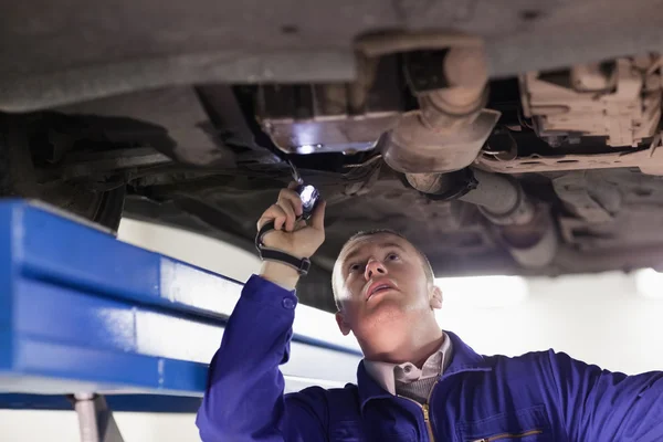 Mechanic looking at a car while holding a flashlight — Stock Photo, Image