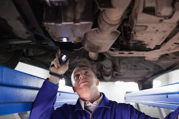 Konzentrierter Mechaniker beleuchtet ein Auto mit einer Taschenlampe — Stockfoto