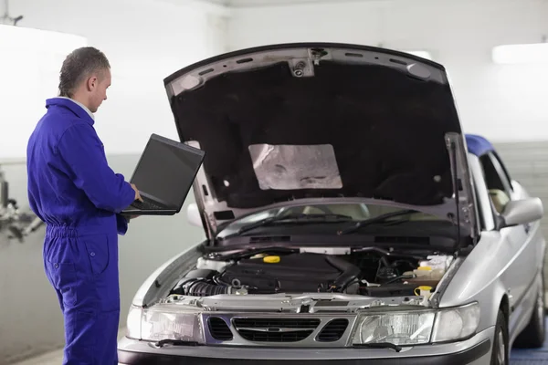 Mechaniker tippt am Computer neben einem Auto — Stockfoto