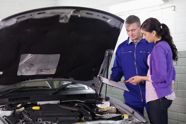 Mechanic standing with a clipboard next to a client — Stock Photo, Image