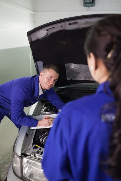 Opierając się na samochód patrząc kolega mechanik — Zdjęcie stockowe