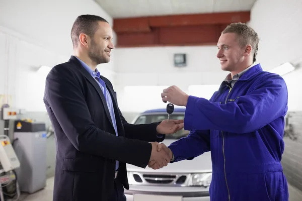 Man receiving car key while shaking hand to a mechanic — Stock Photo, Image