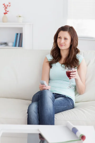 Femme tenant une télécommande et un verre de vin — Photo