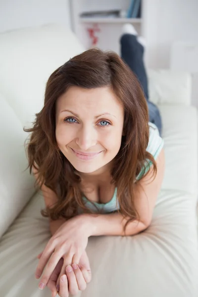 Mujer sonriente acostada sobre el vientre en un sofá —  Fotos de Stock