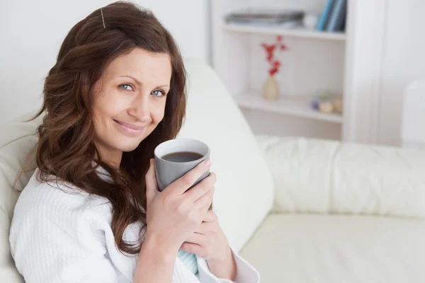 Kvinna sitter på en soffa som innehar en mugg av fika — Stockfoto