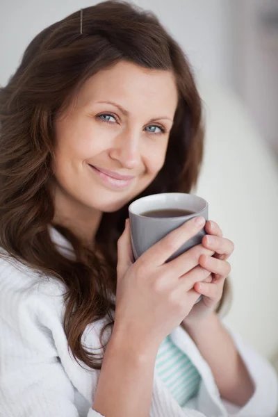 Mulher segurando uma caneca de café enquanto olha para a câmera — Fotografia de Stock