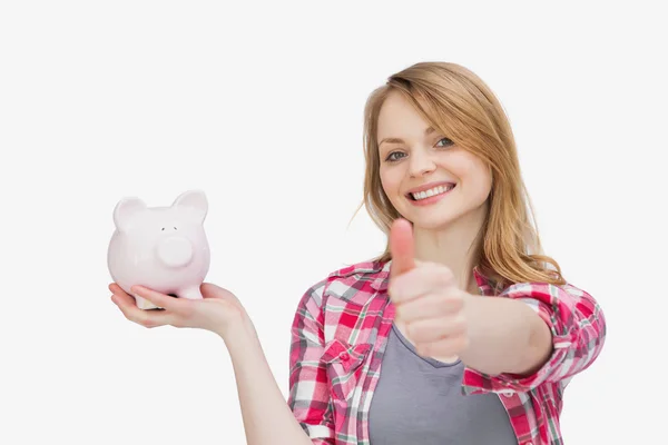 Woman holding a piggy bank with her thumb up — Stock Photo, Image