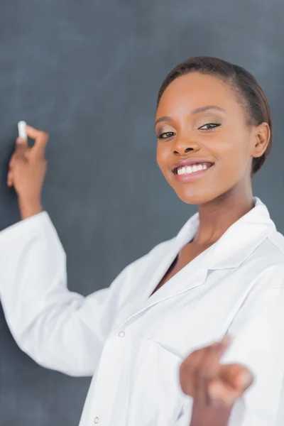 Teacher writing on a blackboard while smiling — Stock Photo, Image