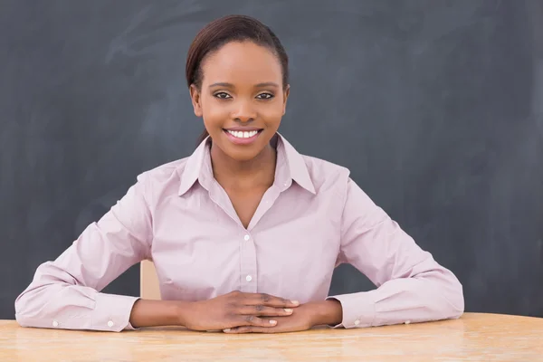 Lehrerin lächelt, während sie ihre Hände auf den Schreibtisch legt — Stockfoto